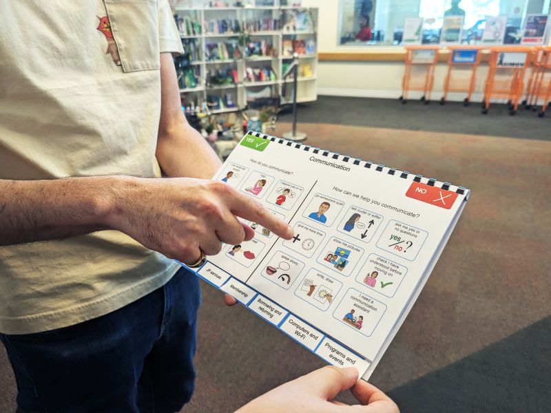 Photograph of West Torrens Library staff member's hands holding an A4 sized communication booklet.