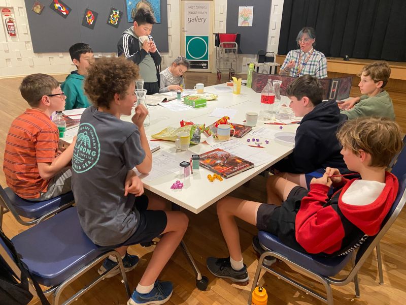 Photograph of older children and a West Torrens Library staff member sitting around a table in the West Torrens auditorium playing Dungeons and Dragons.